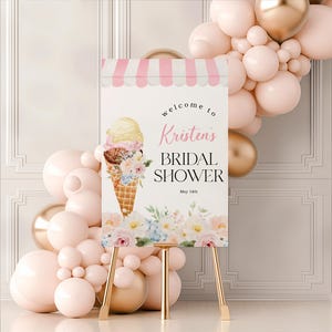 May include: A white welcome sign with pink and white stripes at the top. The sign says "Welcome to Kristen's Bridal Shower May 14th". There is an illustration of an ice cream cone with flowers on the sign.