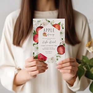 Może przedstawiać: Biała karta zaproszenia z kwiatowym wzorem z czerwonymi jabłkami i białymi kwiatami. Tekst na karcie brzmi "APPLE of my eye" i "Kaylen Russel".