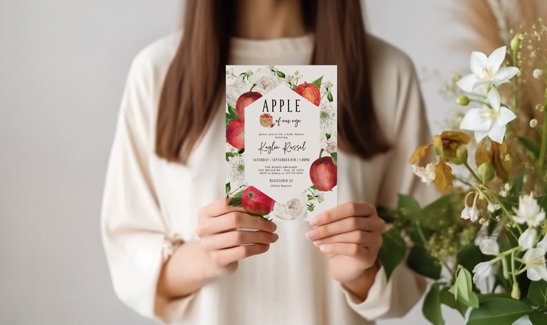 Może przedstawiać: Biała karta zaproszenia z kwiatowym wzorem z czerwonymi jabłkami i białymi kwiatami. Tekst na karcie brzmi "APPLE of my eye" i "Kaylen Russel".