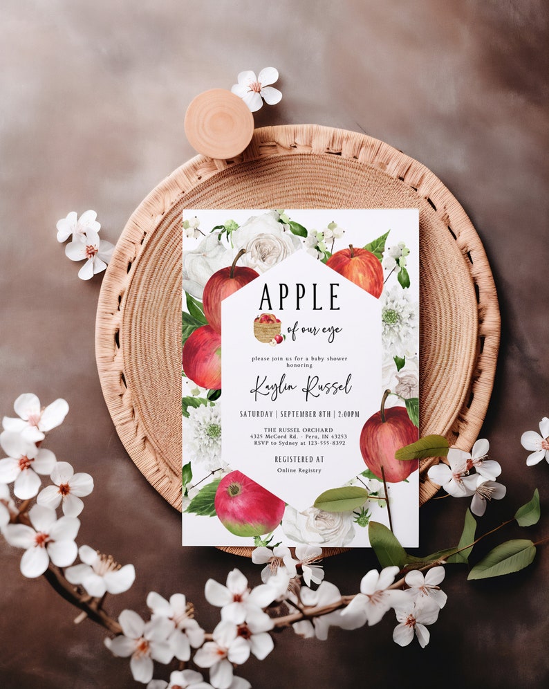 Może przedstawiać: Biała karta z czerwonym wzorem jabłka i tekstem "APPLE of our eye" i "Kaylin Russel" z kwiatową ramką. Karta jest zaproszeniem na baby shower z datą, godziną i miejscem wydarzenia.