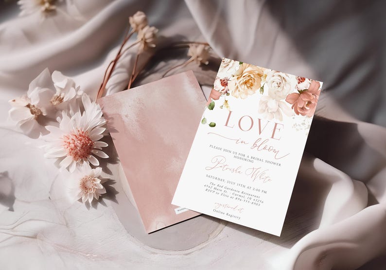 May include: A bridal shower invitation with floral accents and the words "LOVE in bloom." The invitation features a soft color palette of pink, white, and peach. Dried flowers and a pink card are also in the image.