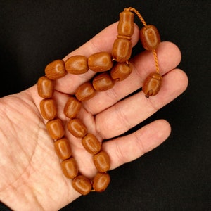 Peut inclure: Un chapelet ou un rosaire en bois brun avec un gland. Les perles sont enfilées sur un cordon fin et sont tenues dans une main.