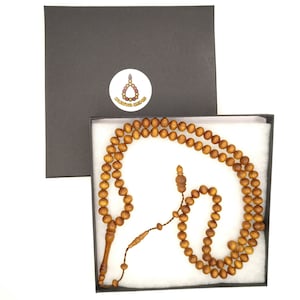 May include: A brown wooden prayer beads mala with a tassel, in a white box with a black lid. The box has a round sticker with the text "DUNYA GEMS".