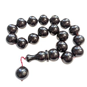 May include: A dark brown prayer bead set, featuring a series of glossy, spherical beads. The beads are strung together with a red cord, and the set includes a longer, decorative bead at the end. The background is plain white.