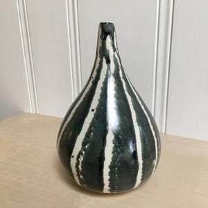 May include: A black and white striped ceramic vase with a pear-shaped body. The vase has a glossy finish and is decorated with irregular white stripes on a dark green background.