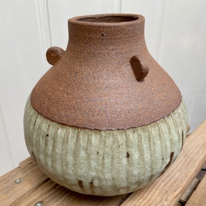 May include: A brown and green ceramic vase with a textured surface. The vase has a rounded body and a wide opening.