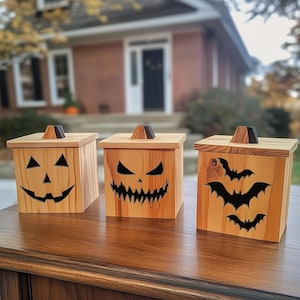 May include: Three wooden boxes with carved jack-o'-lantern faces and bat designs. The boxes are sitting on a wooden table.