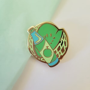 May include: Gold enamel pin featuring a green watermelon slice with a green and blue bottle of soda inside.