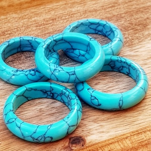 Puede incluir: Cinco anillos turquesa con un patrón de mármol. Los anillos están apilados uno encima del otro sobre una superficie de madera.