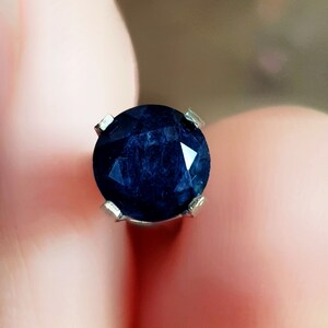 Peut inclure: Une pierre précieuse bleu foncé sertie dans une monture à griffes en argent. La pierre précieuse est ronde et a une taille facetée.