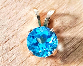 Puede incluir: Un colgante de oro con una piedra preciosa de topacio azul. La piedra preciosa tiene forma ovalada y está tallada a facetas.