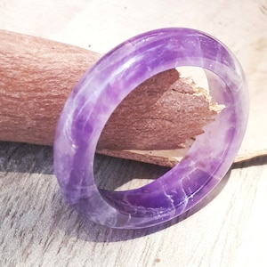 May include: A purple amethyst ring with a smooth, polished finish. The ring is made of natural stone and has a unique, swirling pattern.
