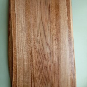 May include: A rectangular wooden cutting board with a natural wood grain finish. The board has a slightly rounded edge and a smooth surface.