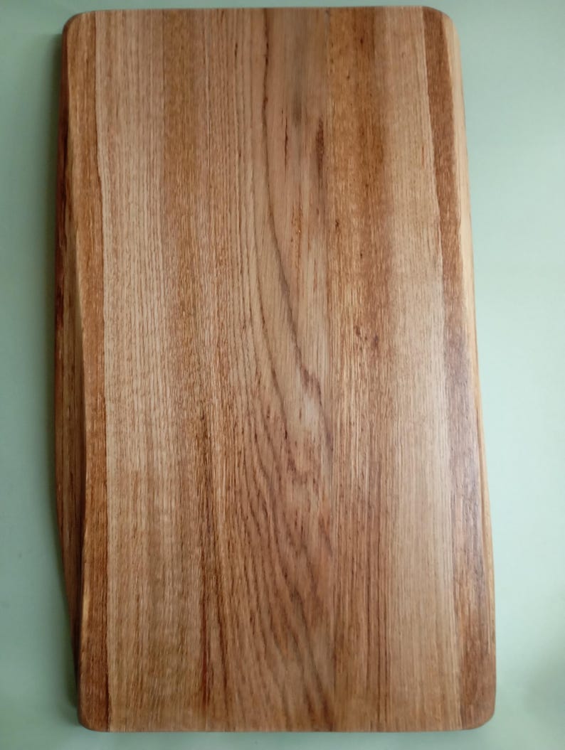 May include: A rectangular wooden cutting board with a natural wood grain finish. The board has a slightly rounded edge and a smooth surface.