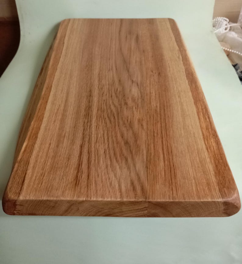 May include: A large, rectangular wooden cutting board with a natural wood finish. The board has a slightly rounded edge and is made of a single piece of wood.