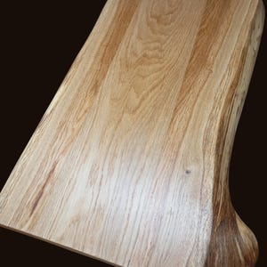 May include: A large, natural wood cutting board with a live edge and a smooth, polished surface. The board is made of light brown wood with a natural grain pattern.
