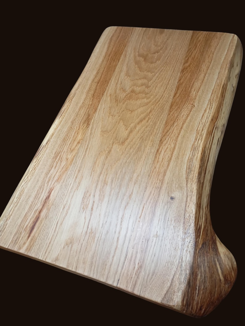 May include: A large, natural wood cutting board with a live edge and a smooth, polished surface. The board is made of light brown wood with a natural grain pattern.