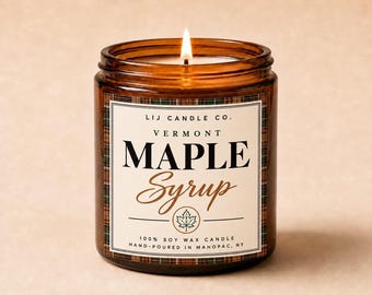 May include: A lit soy wax candle in an amber glass jar with a label reading LIJ CANDLE CO. VERMONT MAPLE SYRUP. The label features a plaid border, a maple leaf icon, and text stating 100% SOY WAX CANDLE HAND-POURED IN MAHOPAC, NY.