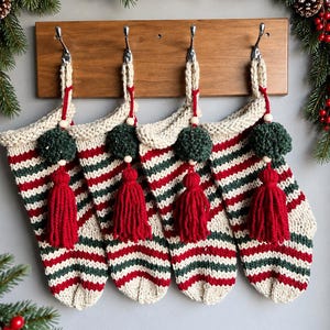 Könnte beinhalten: Vier handgestrickte Weihnachtsstrümpfe mit horizontalen Streifen in Creme, Waldgrün und Rot. Jeder Strumpf ist mit einem cremefarbenen Bündchen, einem dunkelgrünen Pompon, einer naturfarbenen Holzperle und einer langen roten Quaste versehen.