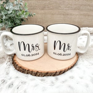 Puede incluir: Dos tazas de cer&aacute;mica blanca con bordes y asas negros. La taza de la izquierda dice "Mrs. 01.06.2024" y la taza de la derecha dice "Mr. 01.06.2024".