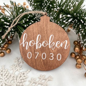 May include: A brown wooden Christmas ornament with the text "hoboken 07030" in white paint.