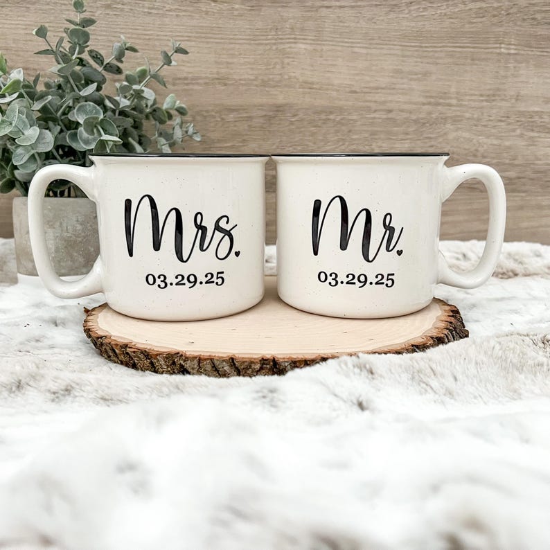 Puede incluir: Dos tazas de cer&aacute;mica blanca con bordes y asas negros. La taza de la izquierda dice "Mrs. 03.29.25" y la taza de la derecha dice "Mr. 03.29.25".