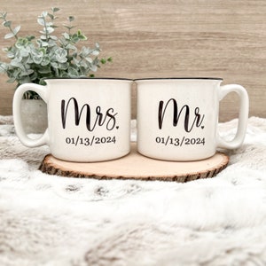 Puede incluir: Dos tazas de cer&aacute;mica blanca con bordes negros y letras negras. La taza de la izquierda dice "Mrs. 01/13/2024" y la taza de la derecha dice "Mr. 01/13/2024".