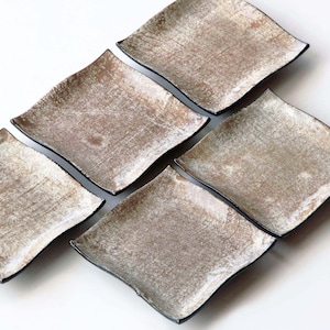 May include: Six square ceramic plates with a textured, off-white surface and a dark rim. The plates are arranged in a diagonal pattern against a white background. The plates have a slightly irregular shape.