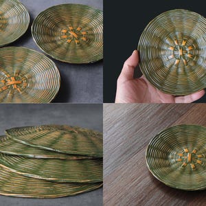 May include: Set of four green and gold ceramic plates with a woven center design. The plates have a ridged texture and a circular shape. The plates are displayed on a dark surface and a wooden surface.