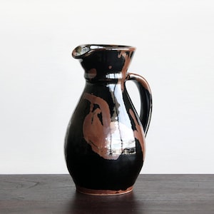 May include: A black ceramic pitcher with a brown glaze. The pitcher has a wide mouth and a handle.