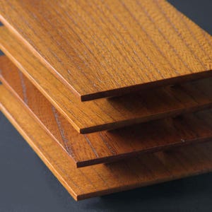 Może przedstawiać: Stos czterech prostokątnych drewnianych desek. Deski mają ciepły, średni brązowy kolor z widocznym usłojeniem drewna. Krawędzie desek są czyste i ostre, a deski są ułożone lekko przesunięte względem siebie.