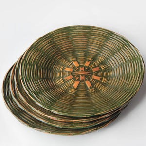 May include: A stack of four green and brown decorative plates. The plates have a woven texture with a circular pattern. The center of each plate features a geometric design in a lighter brown color.