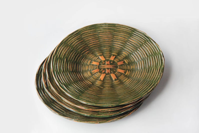 May include: A stack of four green and brown decorative plates. The plates have a woven texture with a circular pattern. The center of each plate features a geometric design in a lighter brown color.