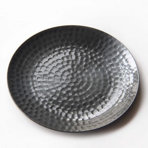May include: A round, dark gray plate with a hammered texture. The plate has a slightly raised edge and a dimpled surface, creating a unique visual appeal. The plate is set against a white background.