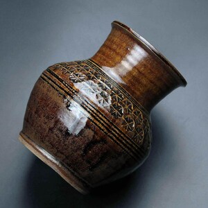 K&ouml;nnte beinhalten: Eine braune Keramikvase mit einem geometrischen Muster in schwarzer Glasur. Die Vase hat eine breite &Ouml;ffnung und einen runden K&ouml;rper.