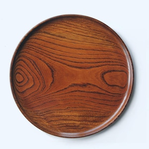 以下が含まれることがあります： 赤茶色の丸い木製サービングトレイ。トレイの表面には顕著な木目模様があり、自然で有機的な美しさを生み出しています。食品の提供や装飾品として最適です。