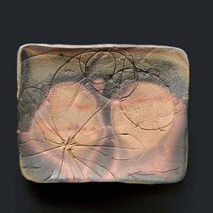 Puede incluir: Un plato cuadrado de cerámica con un diseño en relieve de una flor con un patrón de remolino en tonos de marrón, rosa y gris.