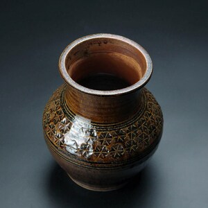 K&ouml;nnte beinhalten: Eine braune Keramikvase mit geometrischem Muster. Die Vase hat eine breite &Ouml;ffnung und einen runden K&ouml;rper.