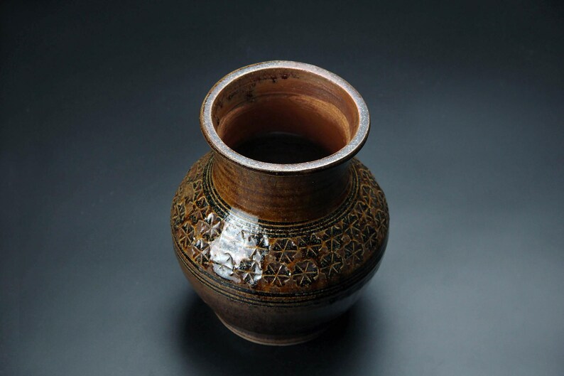 K&ouml;nnte beinhalten: Eine braune Keramikvase mit geometrischem Muster. Die Vase hat eine breite &Ouml;ffnung und einen runden K&ouml;rper.