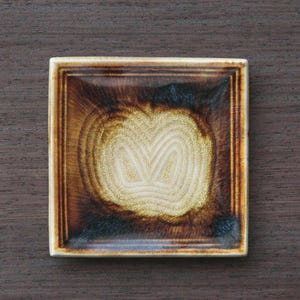 Könnte beinhalten: Eine quadratische Keramikschale mit brauner und weißer Glasur. Die Schale hat ein dekoratives Design in der Mitte.