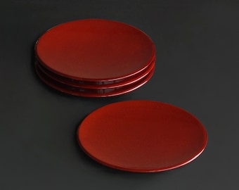 May include: A stack of four and one additional red, round plates. The plates have a glossy finish and are arranged on a dark gray surface. The plates are a solid, vibrant red color.