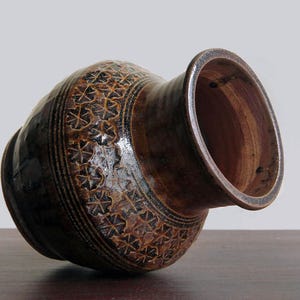 K&ouml;nnte beinhalten: Eine braune Keramikvase mit einem dekorativen Muster aus braunen und schwarzen Bl&auml;ttern. Die Vase hat eine breite &Ouml;ffnung und einen abgerundeten Boden.