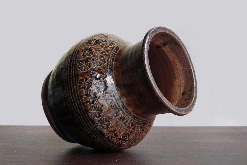 K&ouml;nnte beinhalten: Eine braune Keramikvase mit einem dekorativen Muster aus braunen und schwarzen Bl&auml;ttern. Die Vase hat eine breite &Ouml;ffnung und einen abgerundeten Boden.