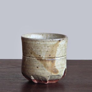 May include: A handmade ceramic cup with a textured, beige exterior and a white interior. The cup features brown and red accents, with a slightly irregular shape. The cup is likely used for drinking beverages.