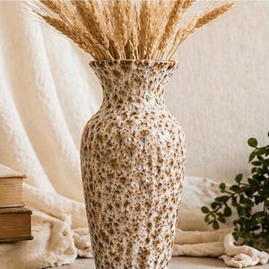 May include: A textured, beige ceramic vase filled with wheat stalks. The vase has a speckled pattern and a wide, flared opening. The wheat is a golden brown color, creating a natural, rustic aesthetic.