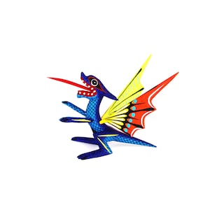 Puede incluir: Figura de dragón de madera pintada a mano. El dragón tiene un cuerpo azul con detalles de escamas, una lengua roja y alas amarillas, rojas y naranjas. Una pieza única de arte popular.