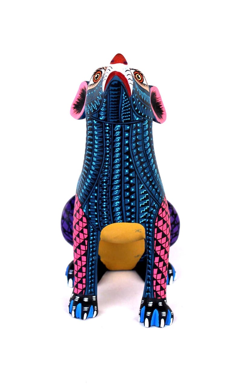 May include: A hand-painted wooden animal figurine featuring a dog-like form with a vibrant blue base color. The surface is covered in intricate geometric patterns in black, white, and pink. It has large ears, pointed eyes, and blue-tipped paws.