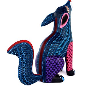 May include: A hand-painted wooden coyote figurine featuring a vibrant color palette of deep blue, bright pink, and purple. The surface is covered in intricate geometric patterns, including small dots, lines, and triangles, with a curved tail.