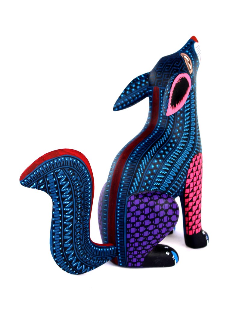 May include: A hand-painted wooden coyote figurine featuring a vibrant color palette of deep blue, bright pink, and purple. The surface is covered in intricate geometric patterns, including small dots, lines, and triangles, with a curved tail.