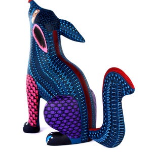 May include: A hand-painted wooden coyote figurine in a howling pose, featuring a deep blue base color with intricate geometric patterns in light blue, pink, purple, and red. The animal has pointed ears, a curved tail, and detailed dot work.